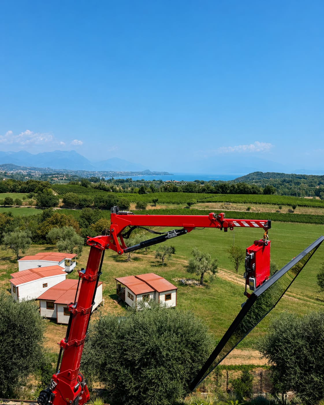 Anta vetrata di grandi dimensioni movimentata con gru durante la posa, vista sul lago di Garda, cantiere CETOS a Lonato